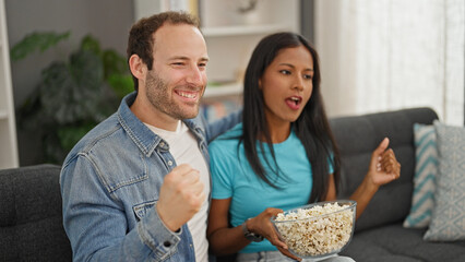 Beautiful couple watching tv eating popcorn celebrating at home