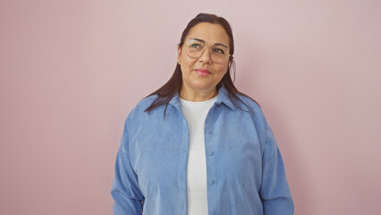 Mature hispanic woman in a blue shirt, smiling against a pink isolated background.