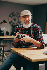 Portrait d'un homme assis photographe hipster situé dans un studio atelier et qui tient un appareil photo vintage en souriant devant un ordinateur - 764952661