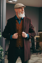 Portrait d'un homme original gentleman quinquagénaire senior hispter élégant et stylé avec un manteau un béret et un gilet dans un atelier créatif - 764953078