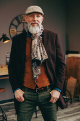 Portrait d'un homme original gentleman quinquagénaire senior hispter élégant et stylé avec un manteau un béret et un gilet dans un atelier créatif - 764953215
