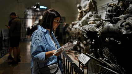 Naklejka premium Young beautiful hispanic woman visiting crypt reading brochure at Imperial Crypt in Vienna