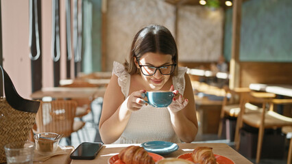 Cheerful, beautiful hispanic woman enjoying a cup of hot caffeine-filled coffee in a sunny cafe,...