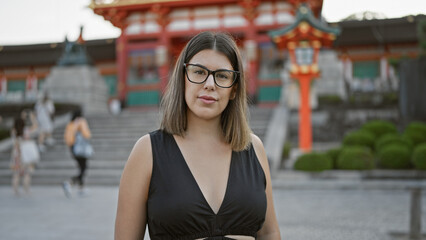 Beautiful latin brunette donning glasses, serious gaze fixated on fushimi inari-taisha shrine,...