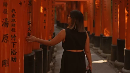 Tuinposter Captivating view of a beautiful hispanic woman in glasses, lost in the mesmerizing walk through the vibrant orange torii gates at fushimi, embodying the essence of traditional japanese culture. © Krakenimages.com