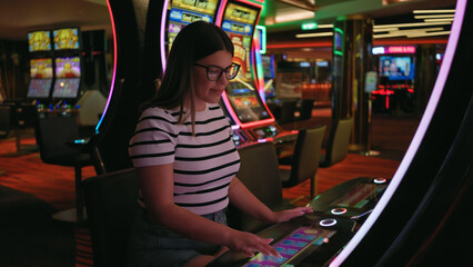 A young adult woman playing a touchscreen electronic game in a vibrant casino setting.