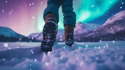Crédence de cuisine en verre imprimé Aurores boréales Close-up view of a hiker’s feet in snow field with beautiful aurora northern lights in night sky in winter.