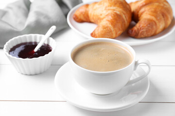 Fresh croissants, jam and coffee on white wooden table. Tasty breakfast
