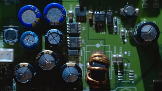 A printed circuit board with many microchips, capacitors and other radio components that cast shadows that follow the light source. Closeup. Macro