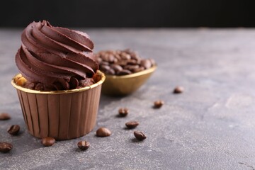 Delicious chocolate cupcake and coffee beans on grey textured table, closeup. Space for text