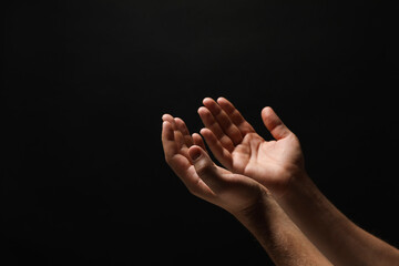 Religion. Man with open palms praying on black background, closeup. Space for text