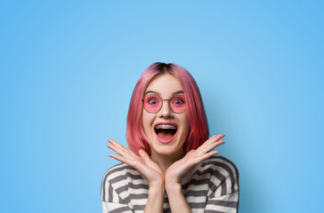 Excited surprised shock astonished very happy pink woman wear braces brackets sunglasses eye glass spectacles, open mouth, hold hands palms near face, isolated blue background. Mega sales ad concept