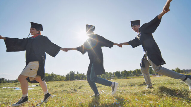 College graduates holding hands run in a round dance.