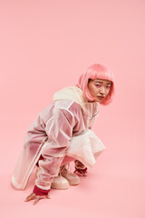 cute asian woman in 20s with pink hair in stylish outfit crouched down against vibrant background