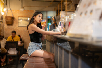 A young woman is sipping a cold alcoholic drink. While sitting at the bar in a rustic cafe and...