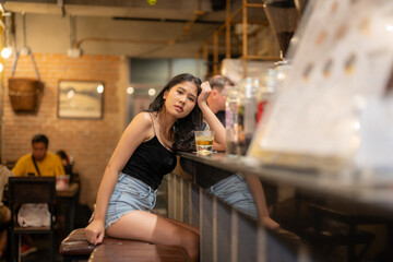 A young woman is sipping a cold alcoholic drink. While sitting at the bar in a rustic cafe and...