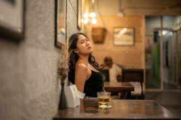 A woman drinks alone at a wooden table in a warmly lit cafe.