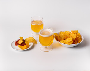 A bowl of chips and a glass of beer sit on a white table