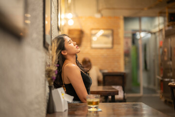 A woman drinks alone at a wooden table in a warmly lit cafe.
