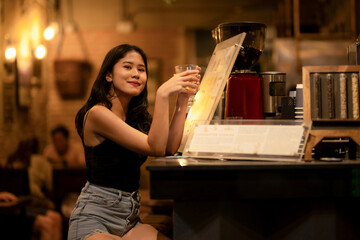 A young woman is sipping a cold alcoholic drink. While sitting at the bar in a rustic cafe and...