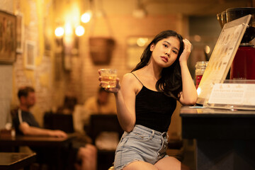 A young woman is sipping a cold alcoholic drink. While sitting at the bar in a rustic cafe and...