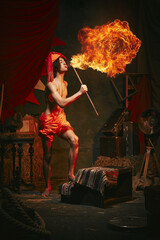 Fire show. Young man in turban breathes fire, displaying dramatic flame burst over dark retro...