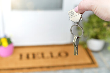 Holding the keys to a new house on the front porch with a HELLO welcome mat.