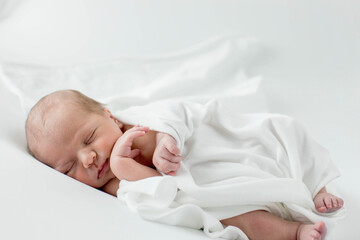 A 3-day-old baby wrapped in white cloth sleeping on a white background