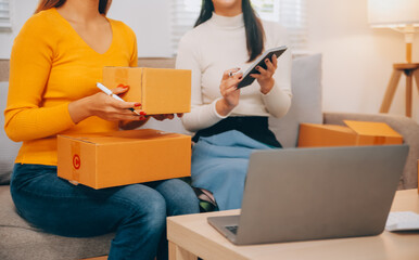 Asian SME business women use laptop computer checking customer order online shipping boxes at home....
