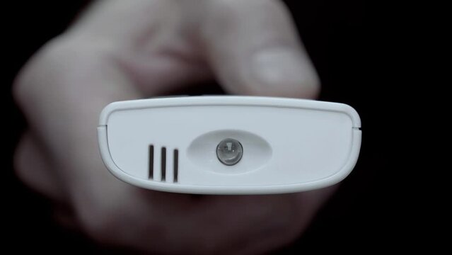 A man's finger presses the on/off button of the air conditioner on a white remote control on a black background. Closeup. Macro. Shot in motion