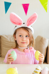 Cute girl wearing bunny ears on Easter day play with Easter eggs at the table at home