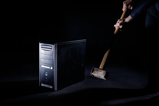 Blow of a large, heavy hammer with a long handle onto a desktop computer, isolated on a black background, slow motion shot. E-waste and technological advancement concepts.