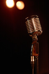 Vertical closeup of retro microphone on stage with lights in background copy space