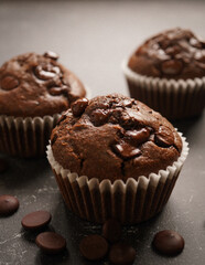 Gluten free chocolate muffins in white muffin's liner with chocolate callets on black marbled background.