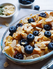 Blueberry bread pudding. Close up almond and blueberry bread pudding on top of a grey napkin. Served with fresh blueberries.