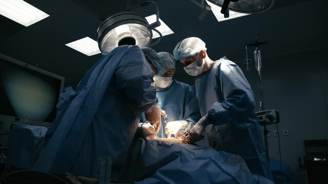 A team of professional surgeons performs an operation on a patient under anesthesia in a modern operating room. The concept of surgical medicine, operations and modern medical technologies.