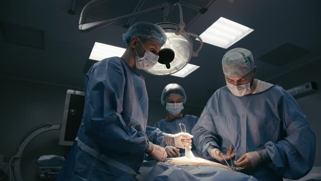 A team of professional surgeons performs an operation on a patient under anesthesia in a modern operating room. The concept of surgical medicine, operations and modern medical technologies.