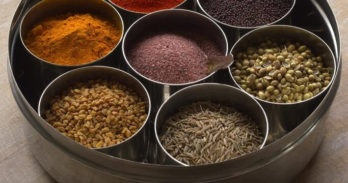 Indian spices box or Indian masala dabba with seven containers and a little spoon on a rustic wooden table. 