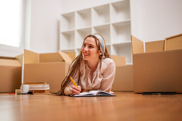 Modern ginger woman with braids writing in notebook while moving in new home.	 - 765026250