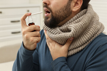 Young man with scarf using throat spray indoors, closeup