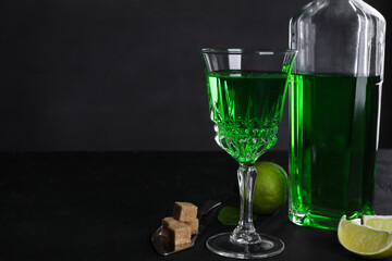 Absinthe, spoon, brown sugar and lime on black table, space for text. Alcoholic drink