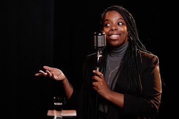 Waist up portrait of young Black woman speaking to microphone performing in stand up show copy space