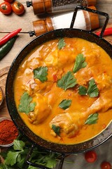 Tasty chicken curry with parsley and ingredients on wooden table, flat lay
