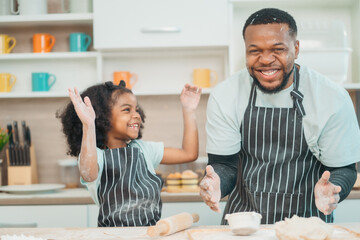 In a home kitchen, black father and his daughter bond over cooking a meal food, their laughter and love filling the air, embodying the joy of African American family life, Father's Day concept - 765031819