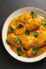 Tasty chicken curry with parsley on black textured table, top view