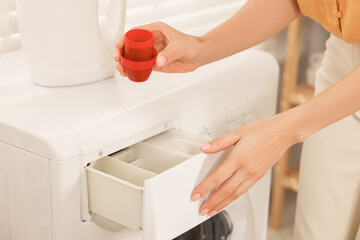 Woman with laundry detergent near washing machine indoors, closeup