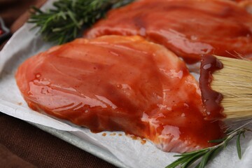 Raw marinated meat, rosemary and basting brush on table, closeup