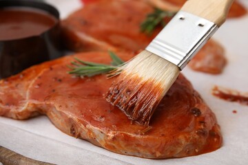 Spreading marinade onto raw meat with basting brush on table, closeup
