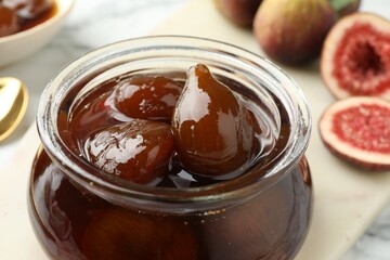 Jar of tasty sweet fig jam on white marble table, closeup