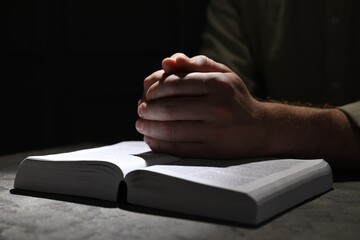 Religion. Christian man praying over Bible at table, closeup. Space for text